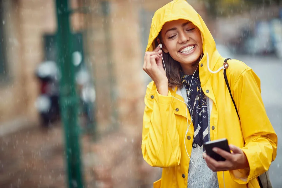 Mujer alegre disfrutando de la lluvia con auriculares con cable