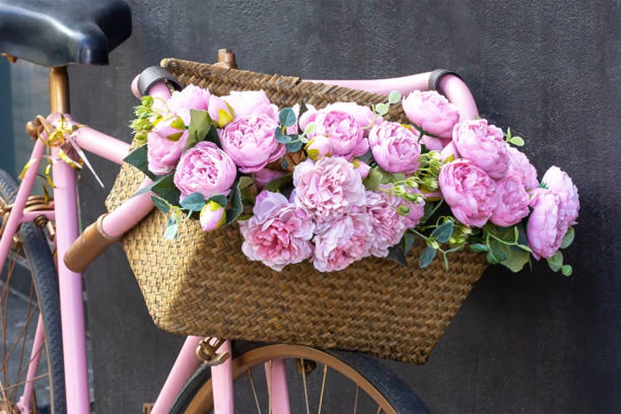 Keranjang sepeda anyaman besar dengan bunga merah muda di dalamnya