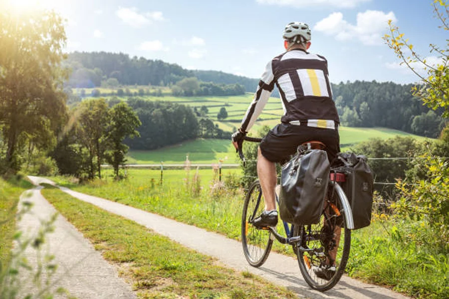 Мужчина ездит на велосипеде по сельской местности с прикрепленными сумками