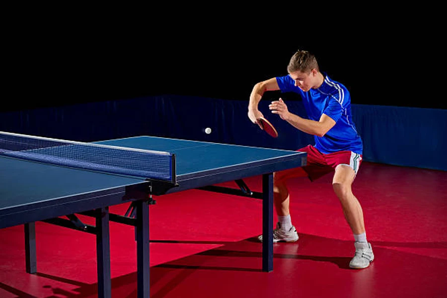 Man hitting white ball across table tennis table indoors