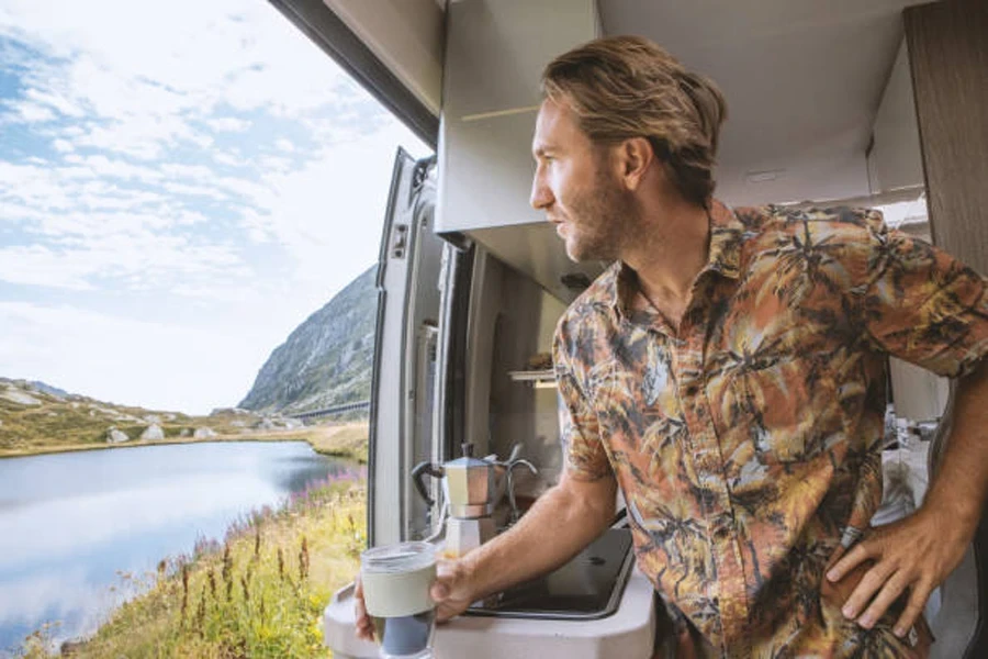 Mann schaut aus seinem Wohnmobil und hält einen Campingbecher in der Hand