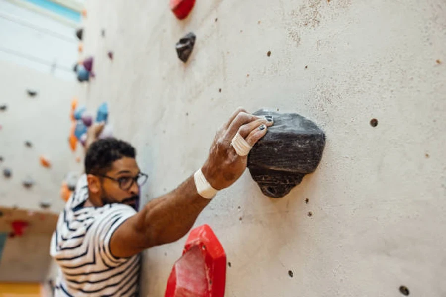 Homem alcançando uma pedra na parede com giz de escalada