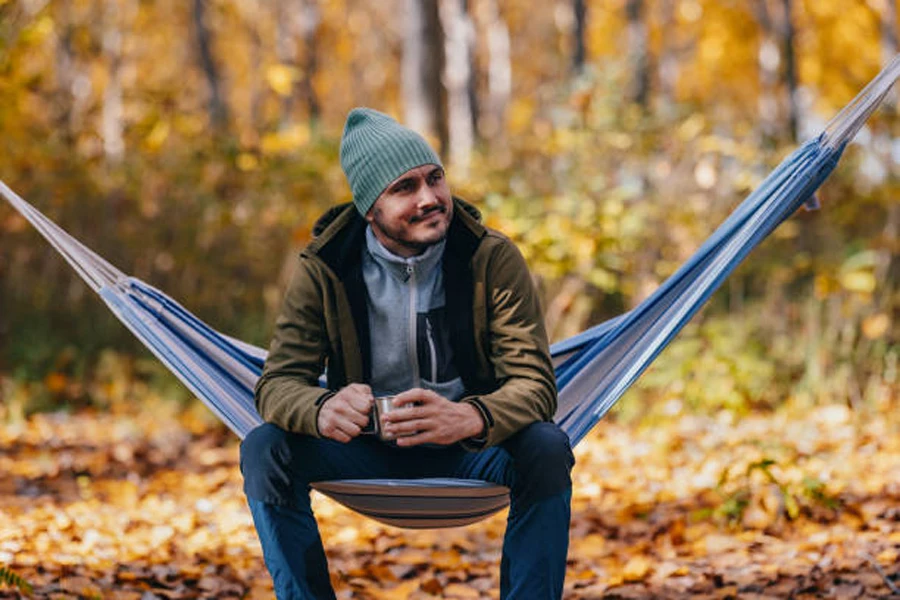 Mann sitzt im Herbst in einer Einzelhängematte aus Segeltuch