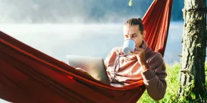 Man sitting in red hammock with laptop and coffee cup