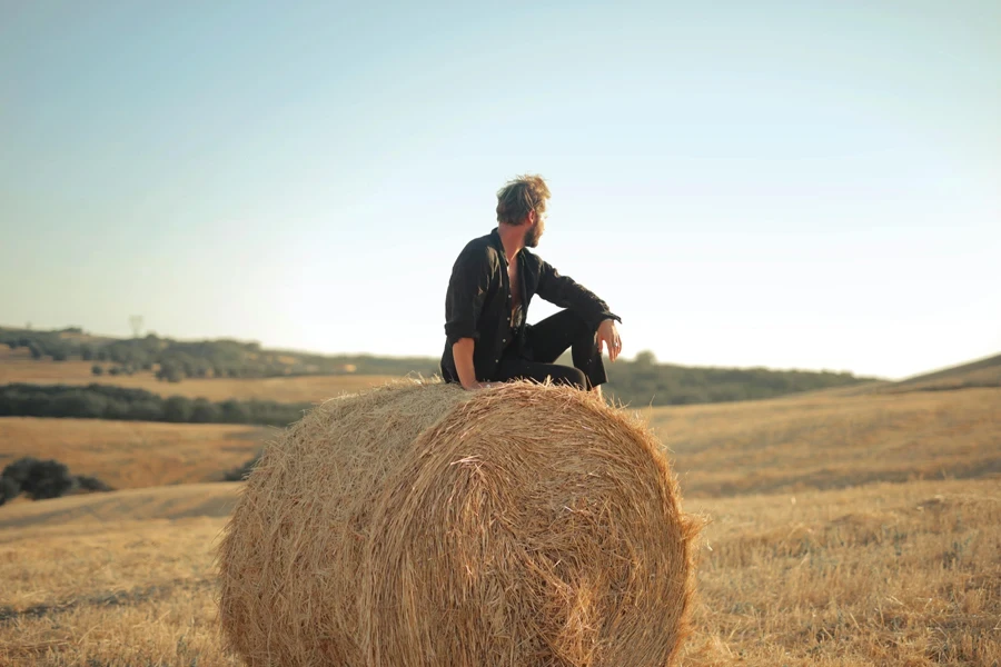 Man sitting on round hay bale looking into the distance