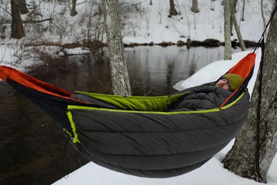 Homme dormant dans un hamac avec un sac de couchage pendant l'hiver