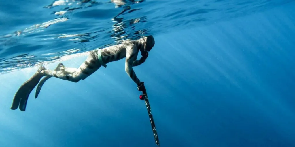 Berrak mavi suda zıpkınla balık avlayan adam