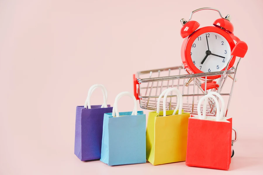 Multicolored shopping bags and alarm clock on pink background