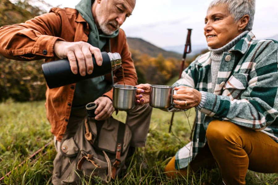 Coppia di anziani che versa il caffè in tazze da campeggio in acciaio inossidabile
