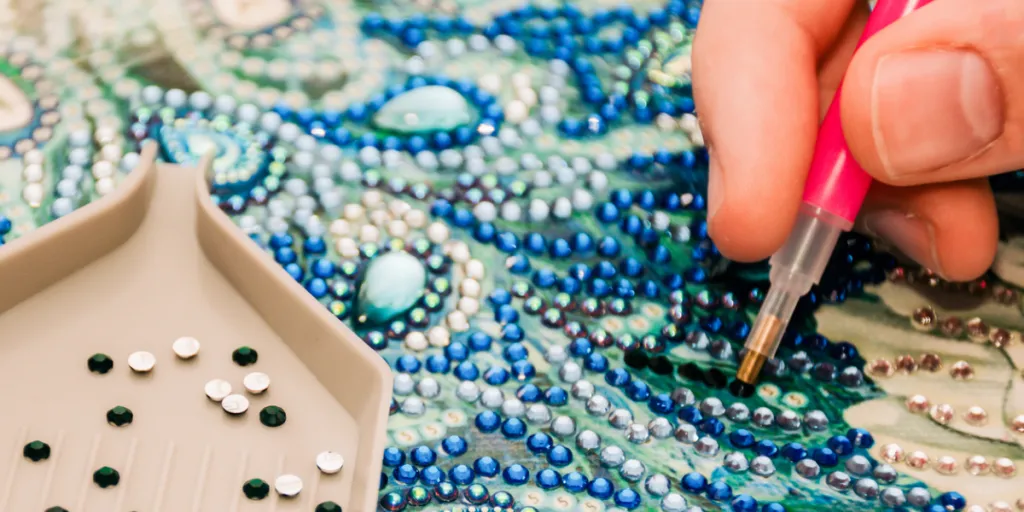 Person applying acrylic rhinestones to an embroidery craft