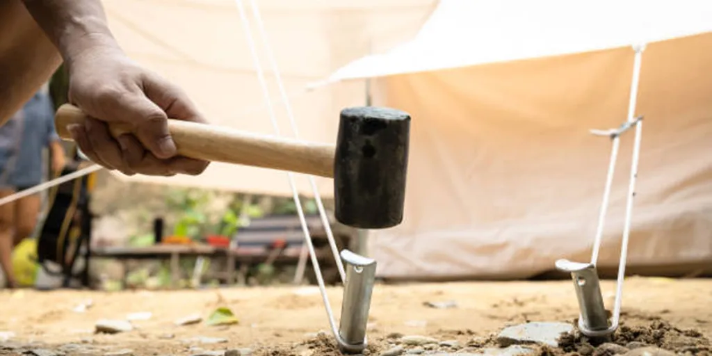 Person hammering pegs into the ground using camping mallet