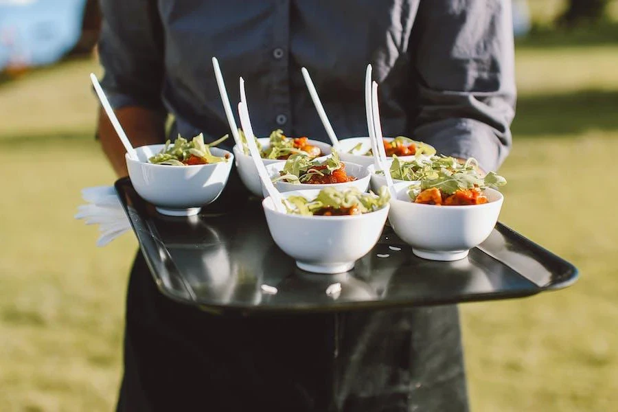 Person holding a tray of white salad bowls