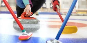 Person releasing curling stone with red handle on ice