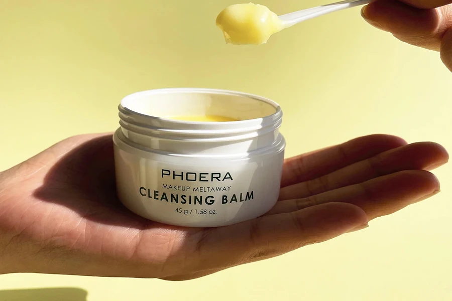Person scooping cleansing balm with a plastic spoon