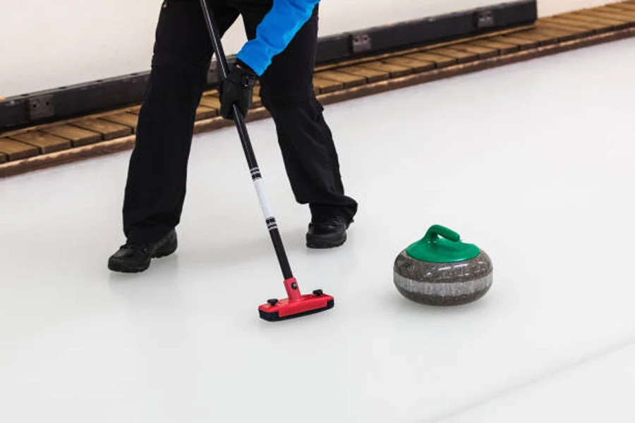Pessoa usando escova de curling para varrer gelo perto da pedra de curling