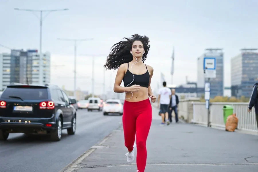 Photo of Woman Listening to Music on Earphones Running Down a Sidewalk