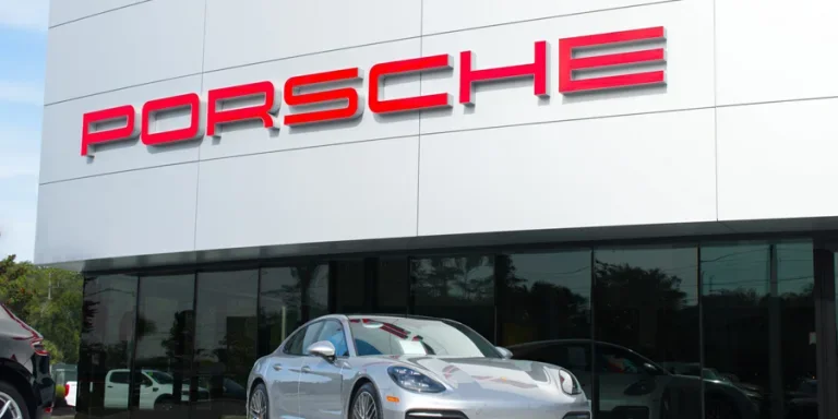 Porsche dealership with red logo on front of building and blue sky background