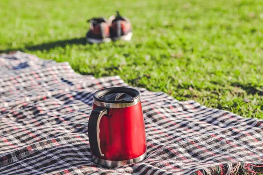 Red insulated camping mug on picnic blanket