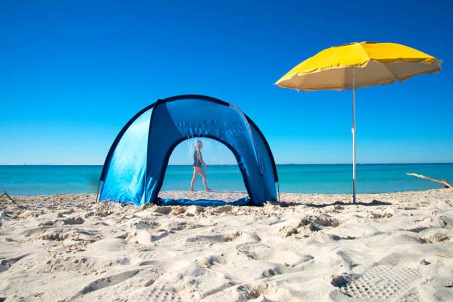 Small blue pop-up beach tent next to yellow umbrella