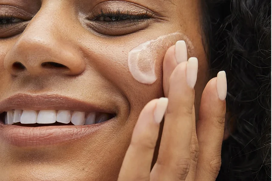 Smiling lady applying primer on her cheek