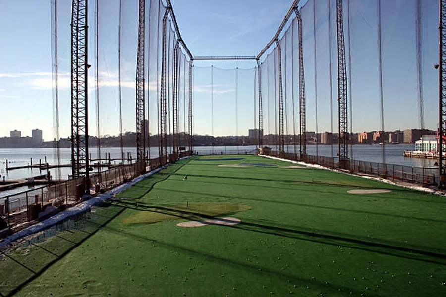 Tall golf driving range net next to river in city