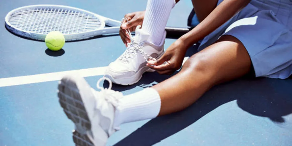 Tennisspieler schnürt weiße Schuhe und sitzt auf dem Tennisplatz