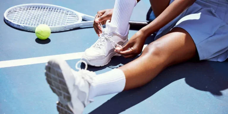 Tennis player lacing up white shoes sitting on tennis court