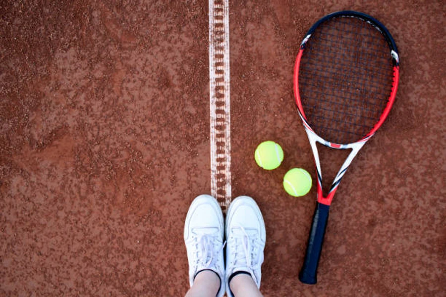 Tennis racquet on clay court next to tennis balls