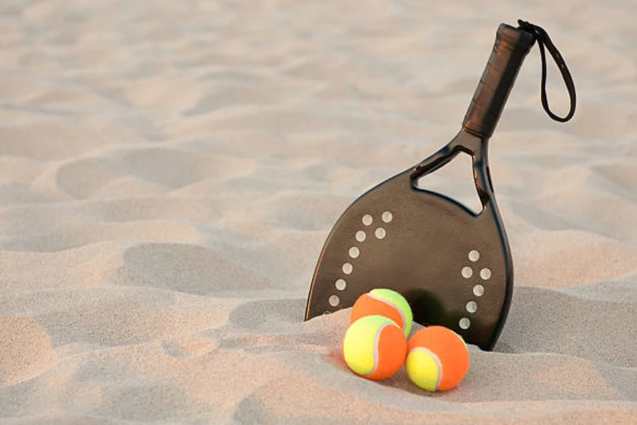 Tres pelotas de tenis de playa en la arena junto a una raqueta negra