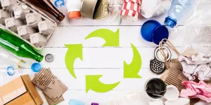 Draufsicht auf verschiedene Müllmaterialien mit Recycling-Symbol auf weißem Holztischhintergrund