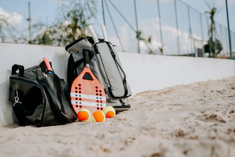 Two beach tennis racket bags and three balls against wall