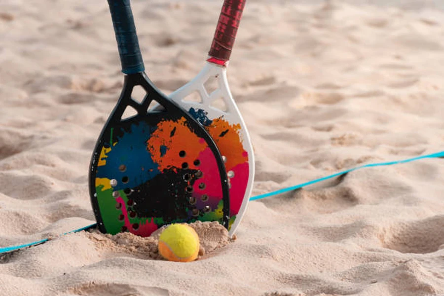 Two beach tennis rackets with ball on sand