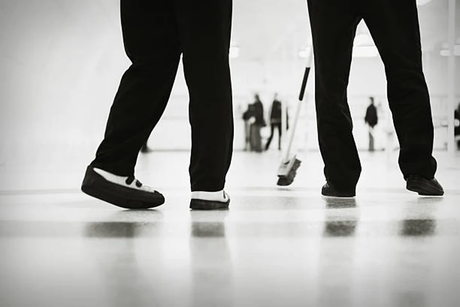 Two curlers wearing black and white curling shoes on ice