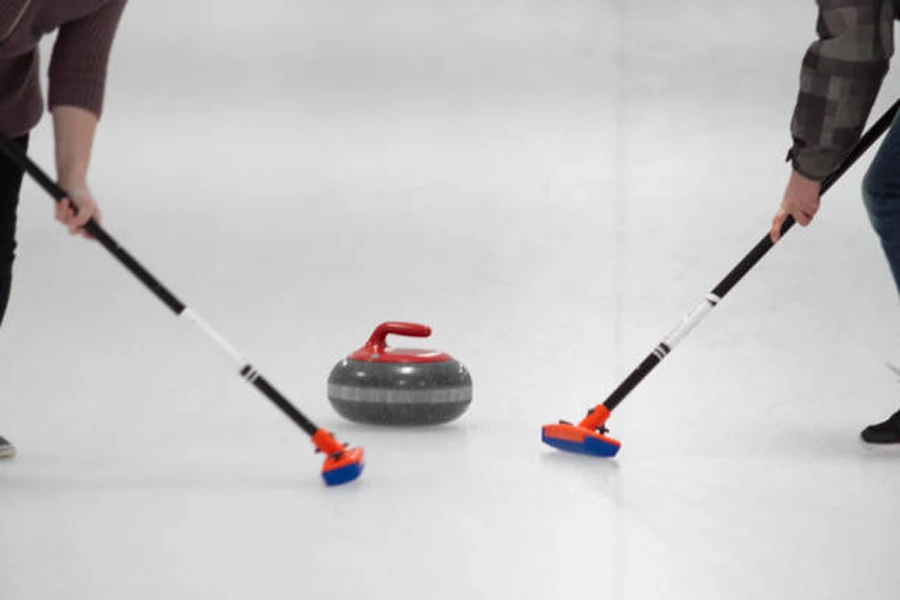 Deux balayeuses sur la patinoire balayant la pierre de curling avec poignée rouge