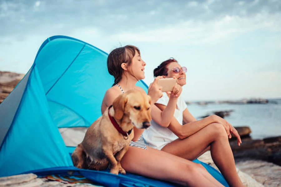 Two women and dog sitting in half-dome tent