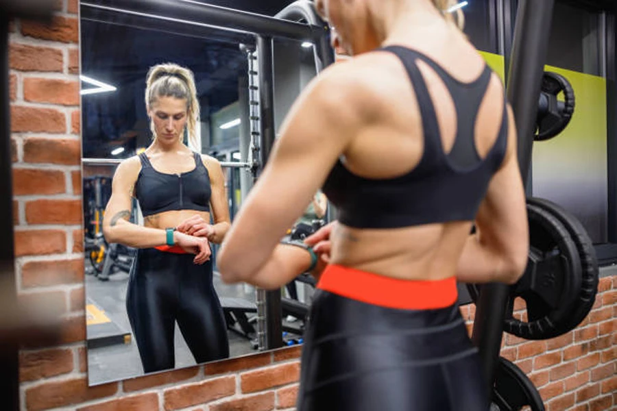 Woman checking watch in front of gym mirror