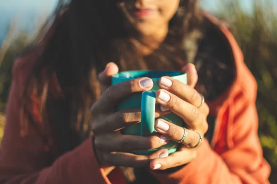 Wanita memegang cangkir berkemah teal di bawah sinar matahari