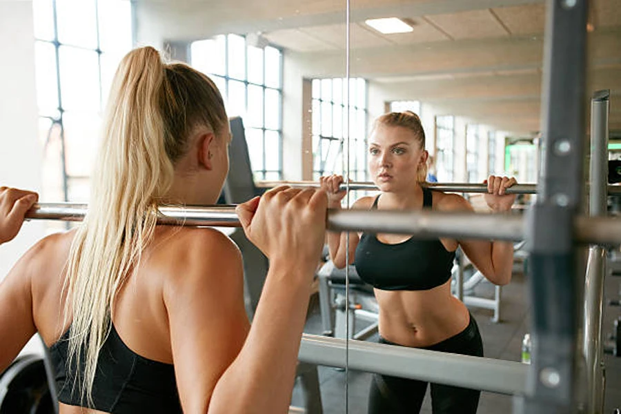 Woman performing back squat in front of gym mirror