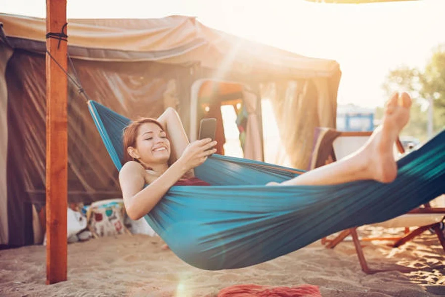 Wanita bersantai di tempat tidur gantung yang didirikan di sebelah tenda pantai