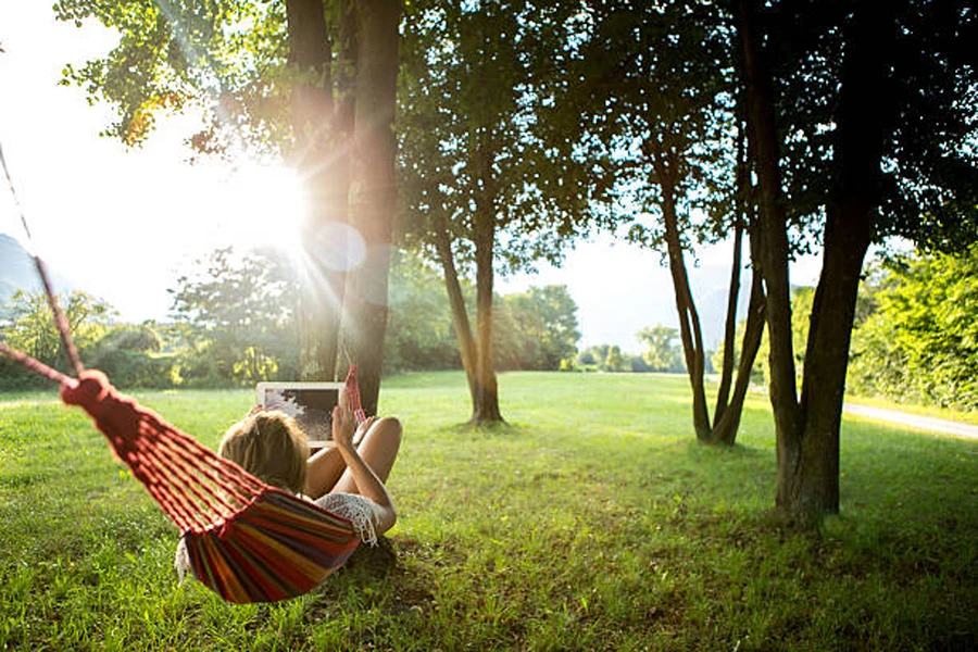 Mujer relajándose con tablet en una hamaca de tela entre árboles