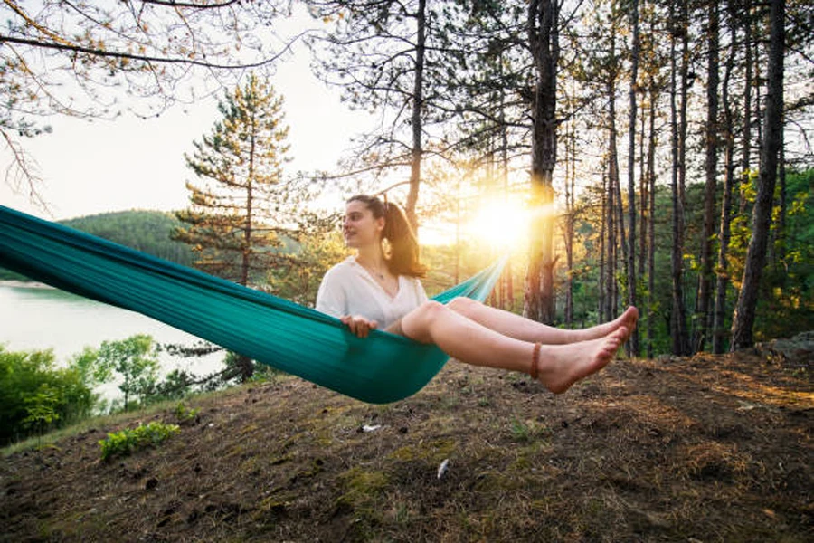 Woman sitting in teal ultra lightweight hammock in forest