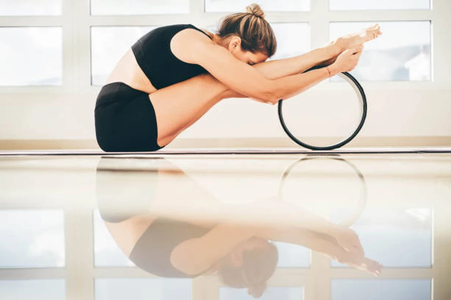 Mulher esticando as pernas enquanto usa roda de ioga de plástico