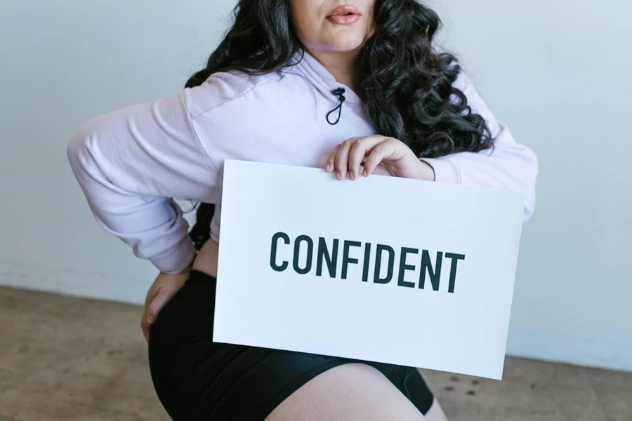 「自信」と書かれた看板を持ったレジャーウェアを着た女性
