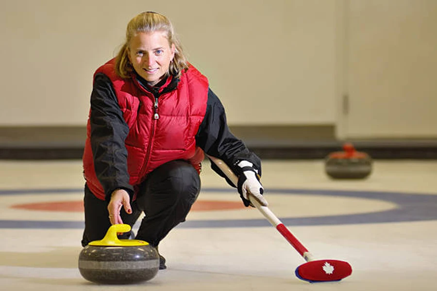 Mulher vestindo colete vermelho enquanto libera curling stone