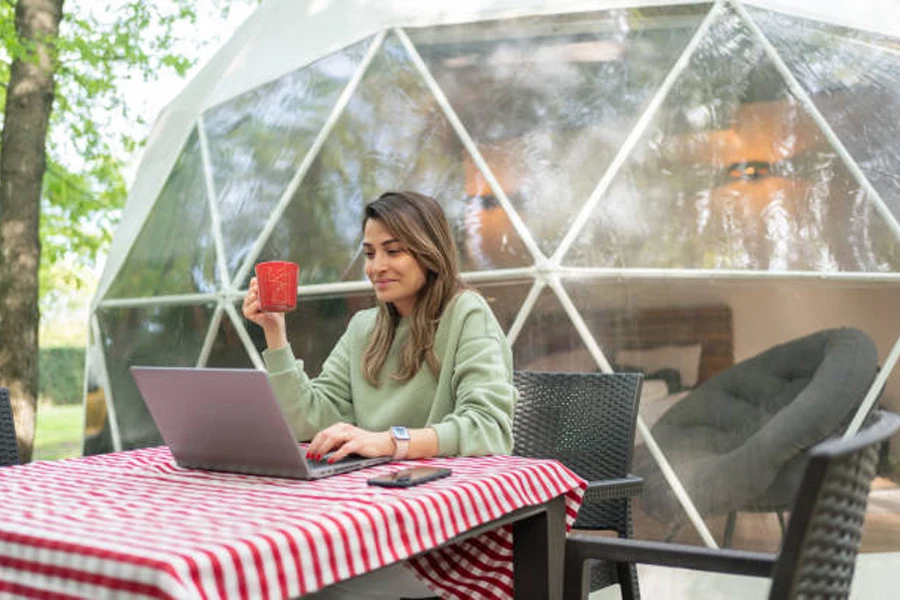 Woman with red cup sitting with laptop at glamping site