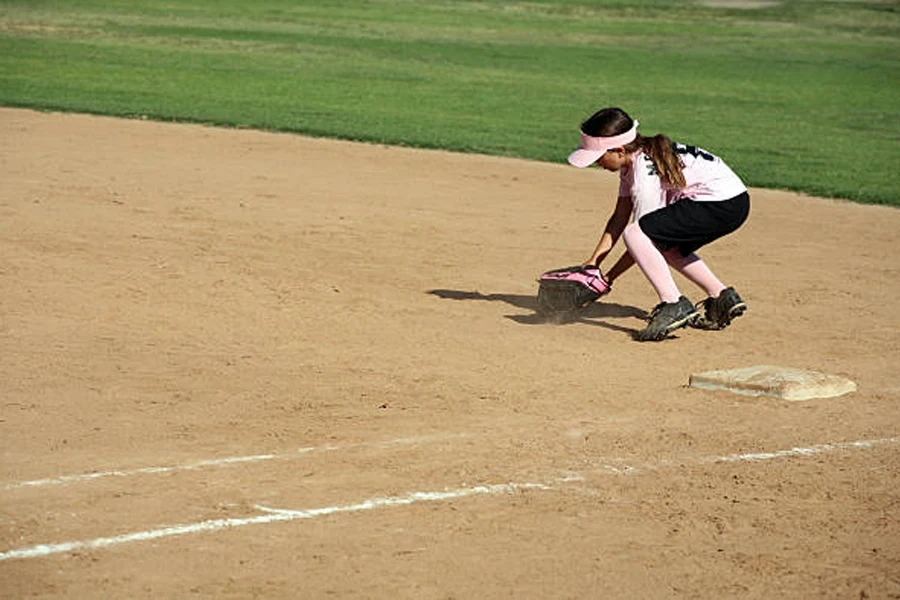 Young girl picking up softball wearing black softball shorts