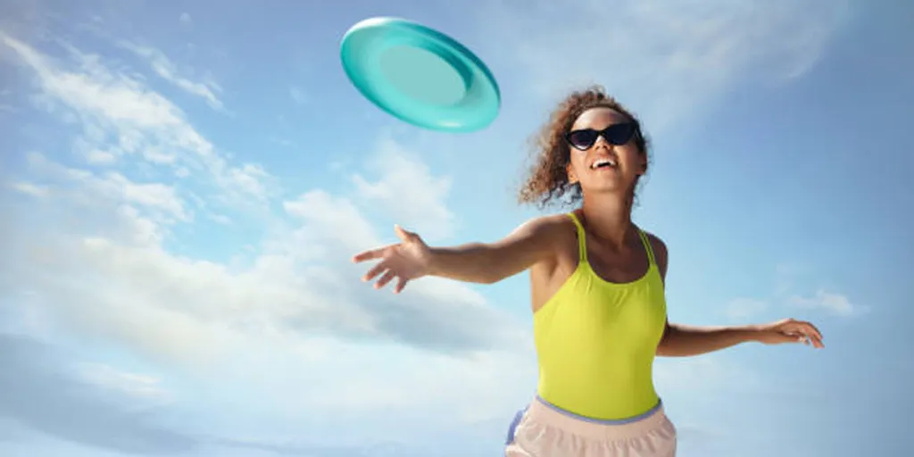 Wanita muda melemparkan frisbee biru muda ke udara