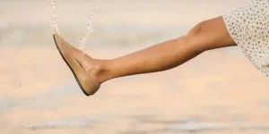 a woman walking on the beach with wet sandals