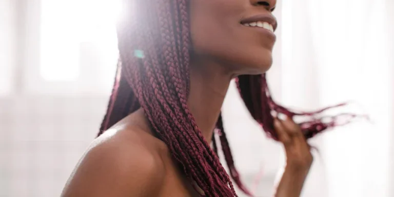 Beautiful smiling African woman standing at bathroom and holding her braided hair