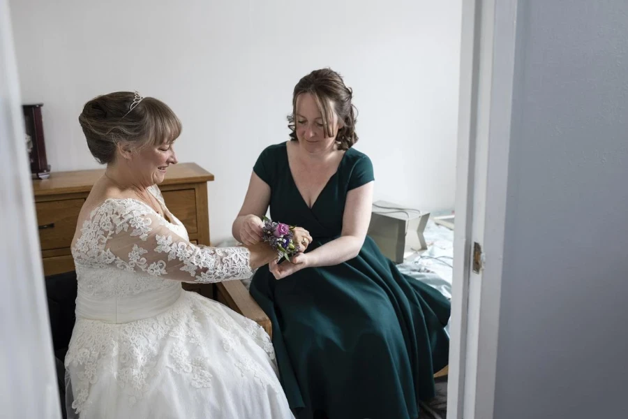 Her daughter is helping her get ready and is putting a flower corsage on her wrist.